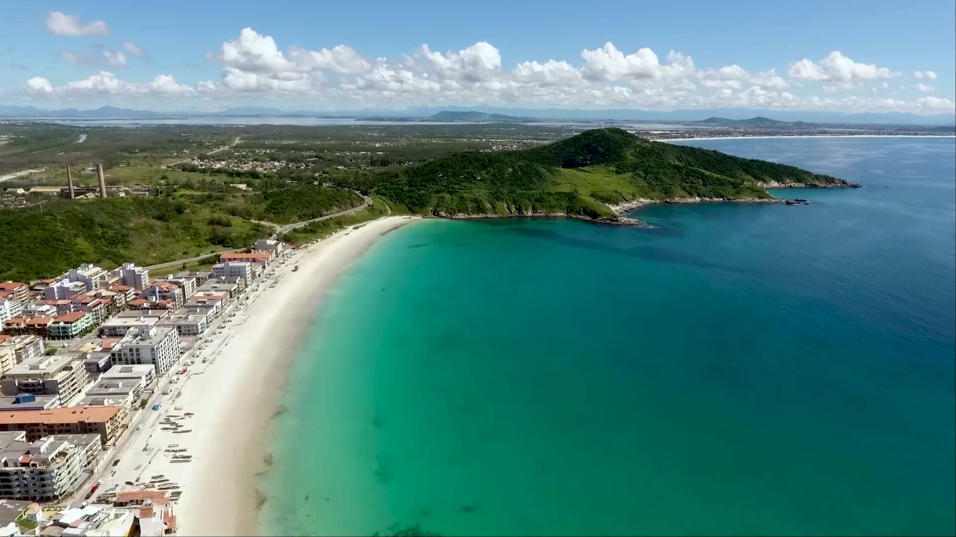 Prainha de Arraial do Cabo vista do drone, com as águas verde-esmeralda entre morros e o mar calmo