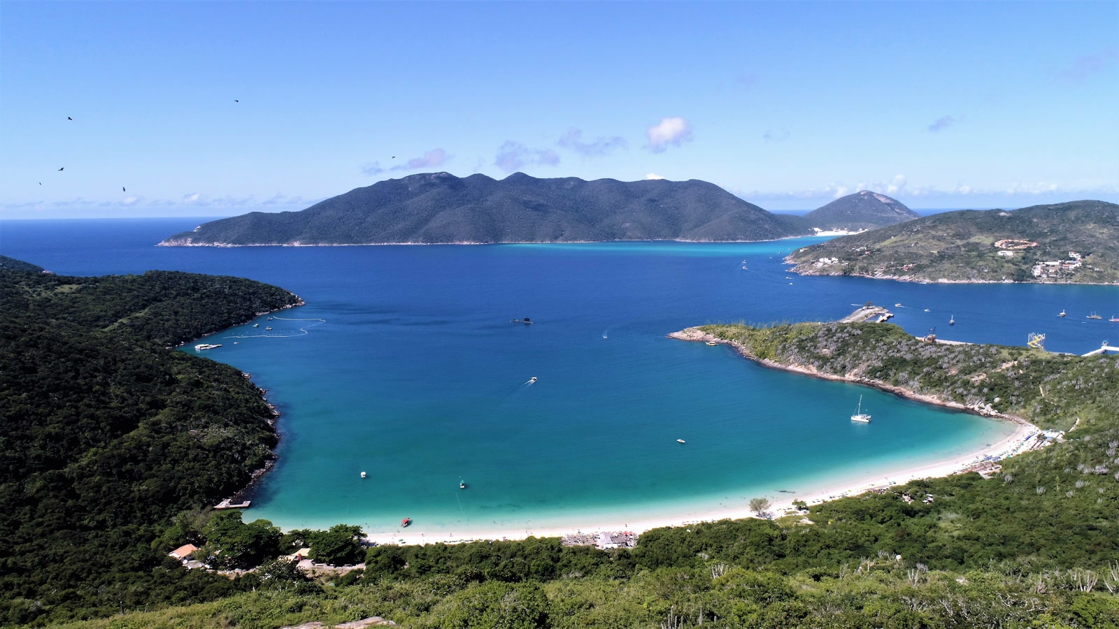 Vista panorâmica da enseada do Forno em Arraial do Cabo, com morros verdes e mar azul-turquesa