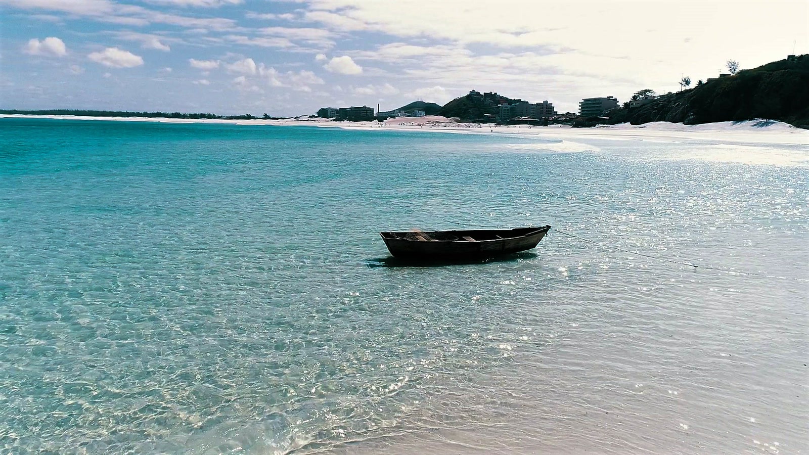 Agua cristalina y transparente de la Praia Grande en Arraial do Cabo, con un pequeño barco de madera