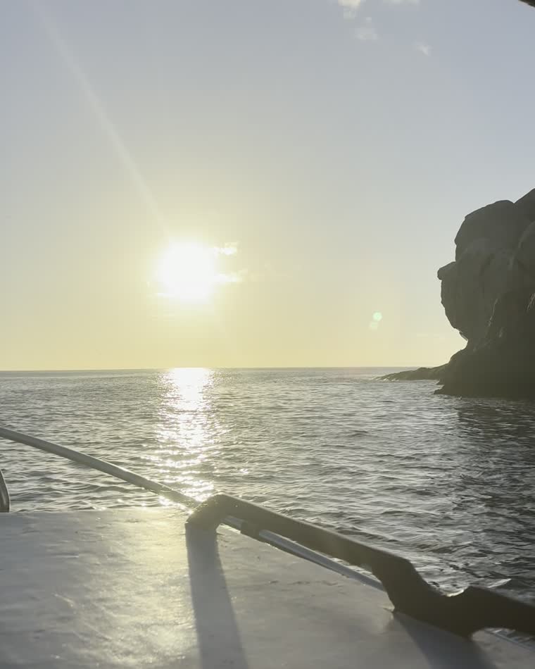 Silhueta de rosto na rocha do Perfil do Guardião, vista do barco com o sol baixo sobre o mar