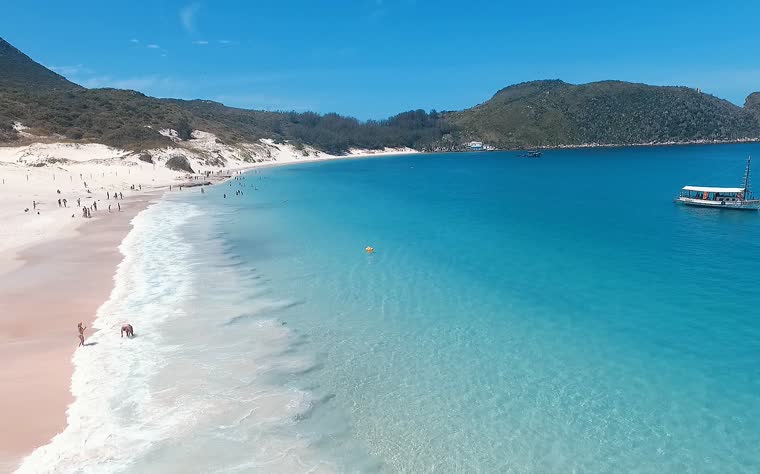 Faixa de areia branca da Ilha do Farol com mar azul-claro e um barco ancorado ao largo