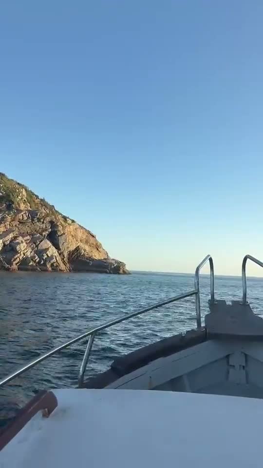 Proa do barco cortando o mar ao entardecer, com o costão ao fundo