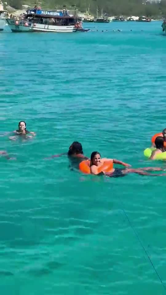 Banhistas nadando com boias na água turquesa ao lado dos barcos