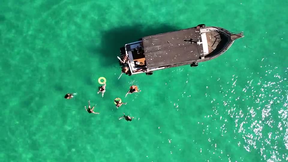 Vista aérea do barco parado em água turquesa com pessoas nadando ao redor